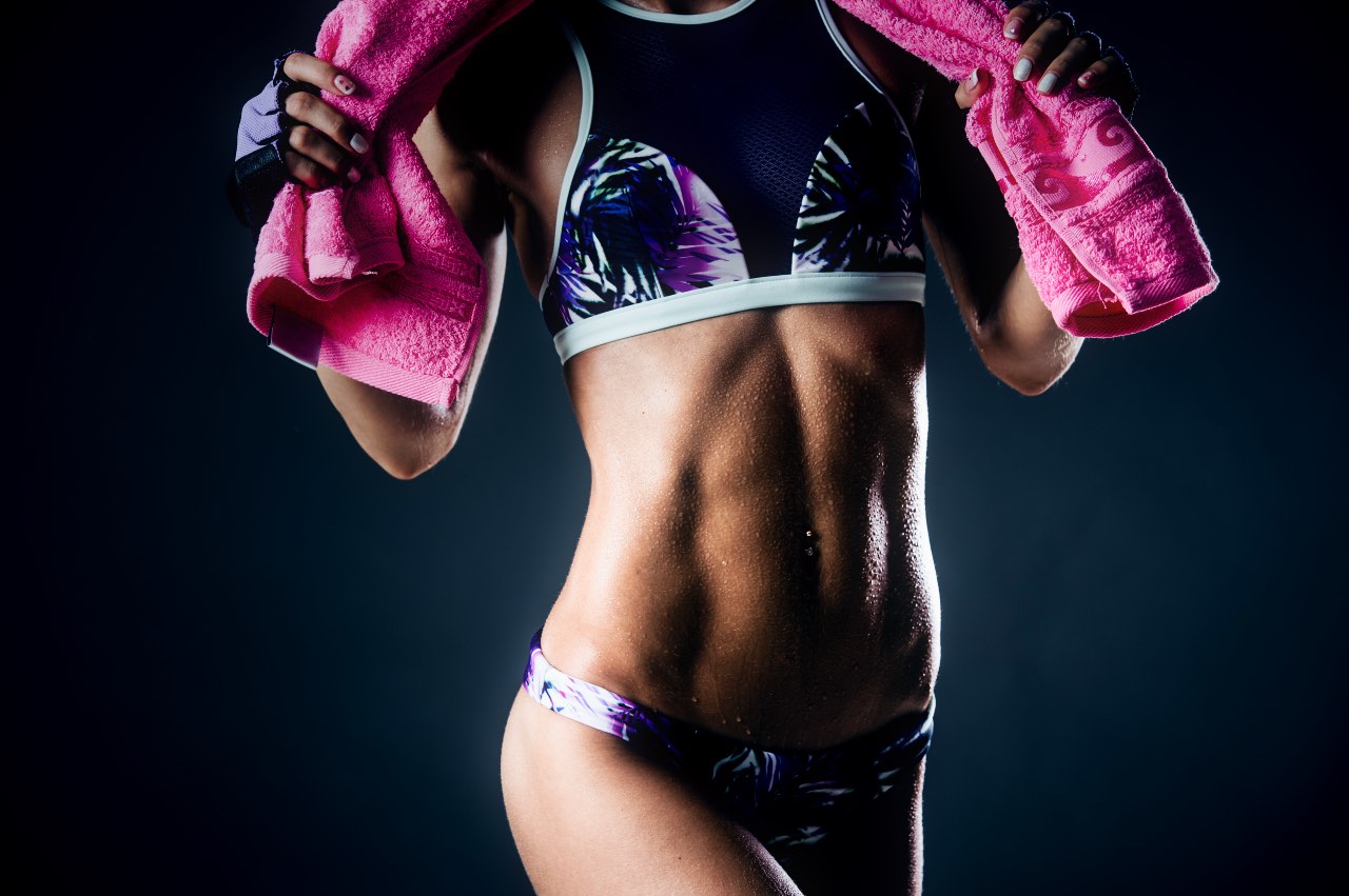 Fit woman posing with a pink towel on dark background